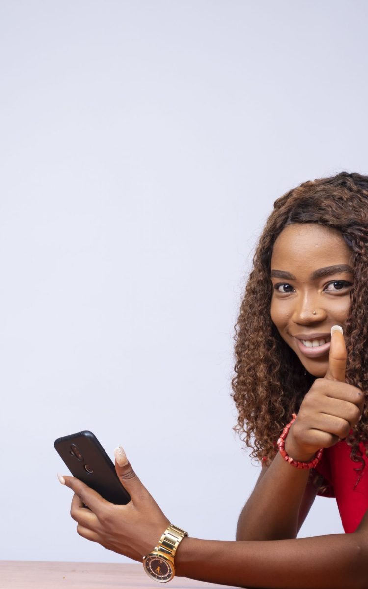 A beautiful black woman sitting sideways, holding her phone and a thumbs up